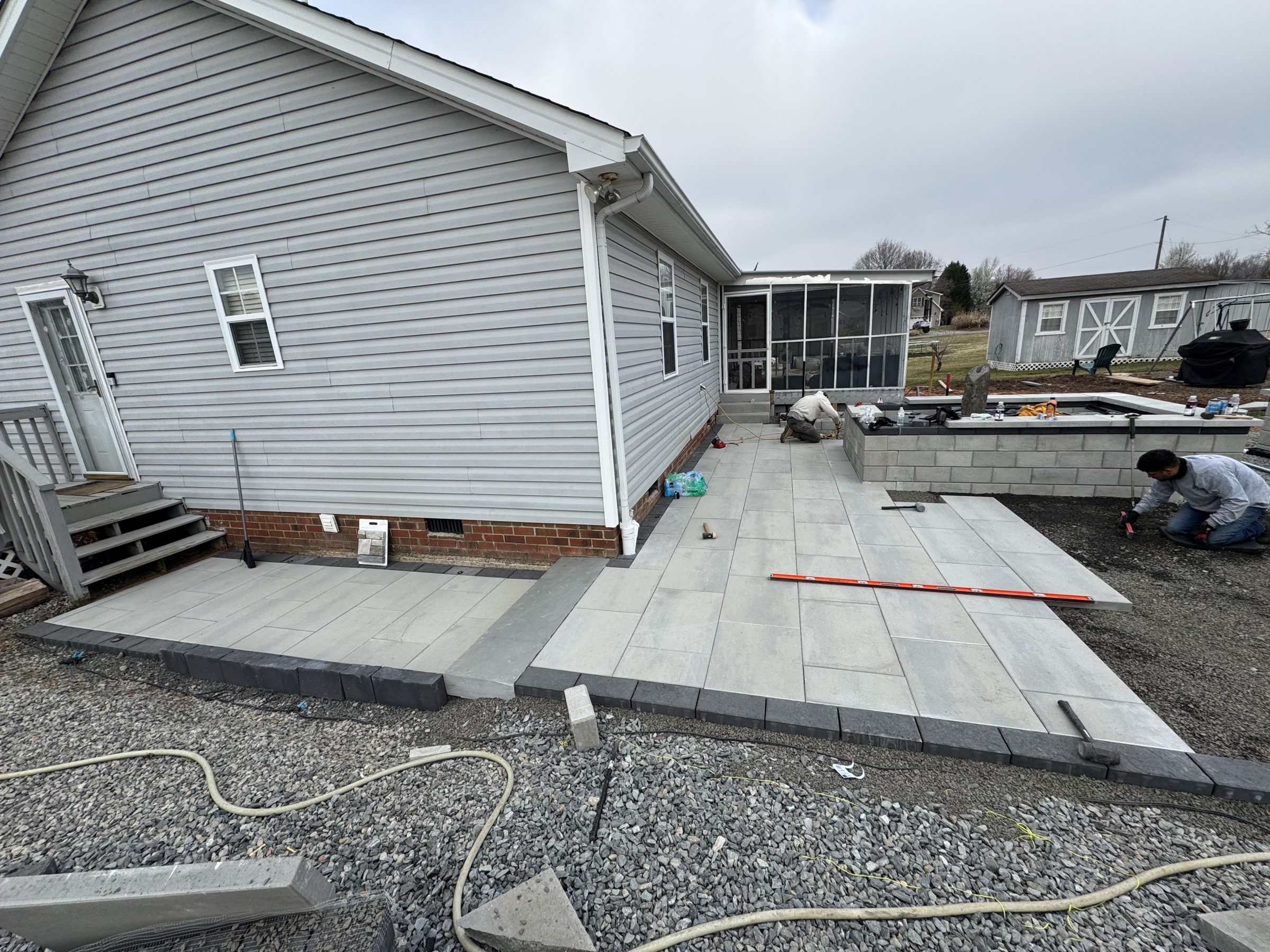 Workers installing a gray paver patio beside a house
