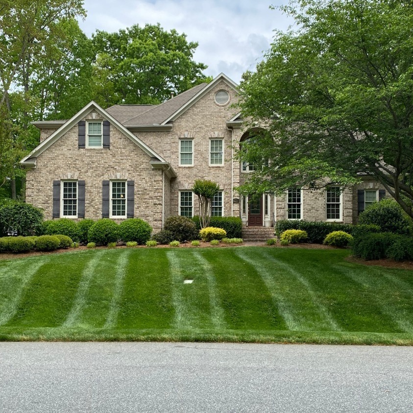 Large brick home with striped lawn and mature trees