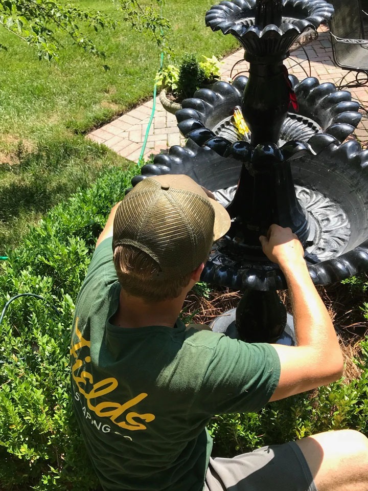 Person assembling black tiered garden fountain outdoors