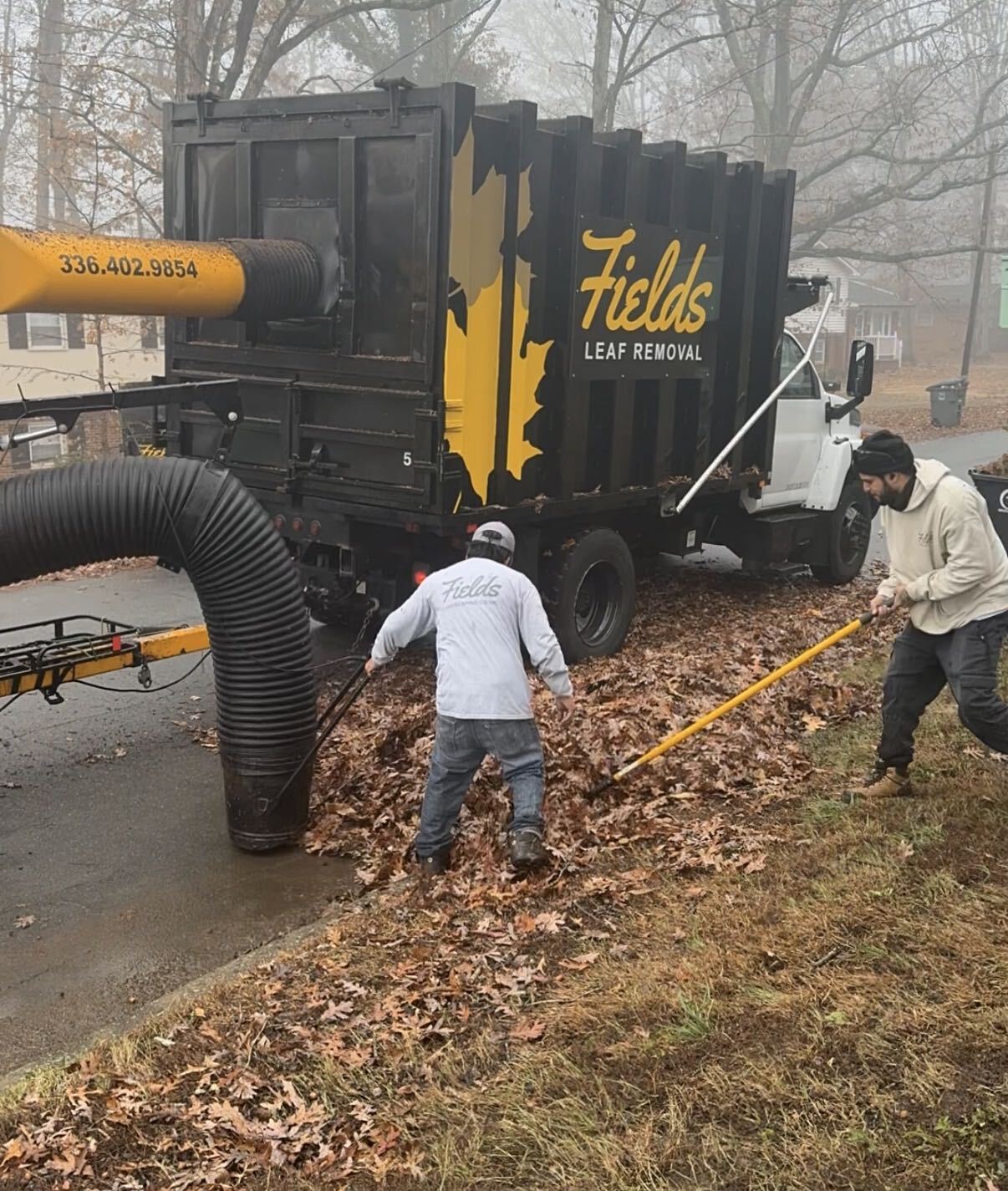 Workers vacuum and rake leaves beside a collection truck.