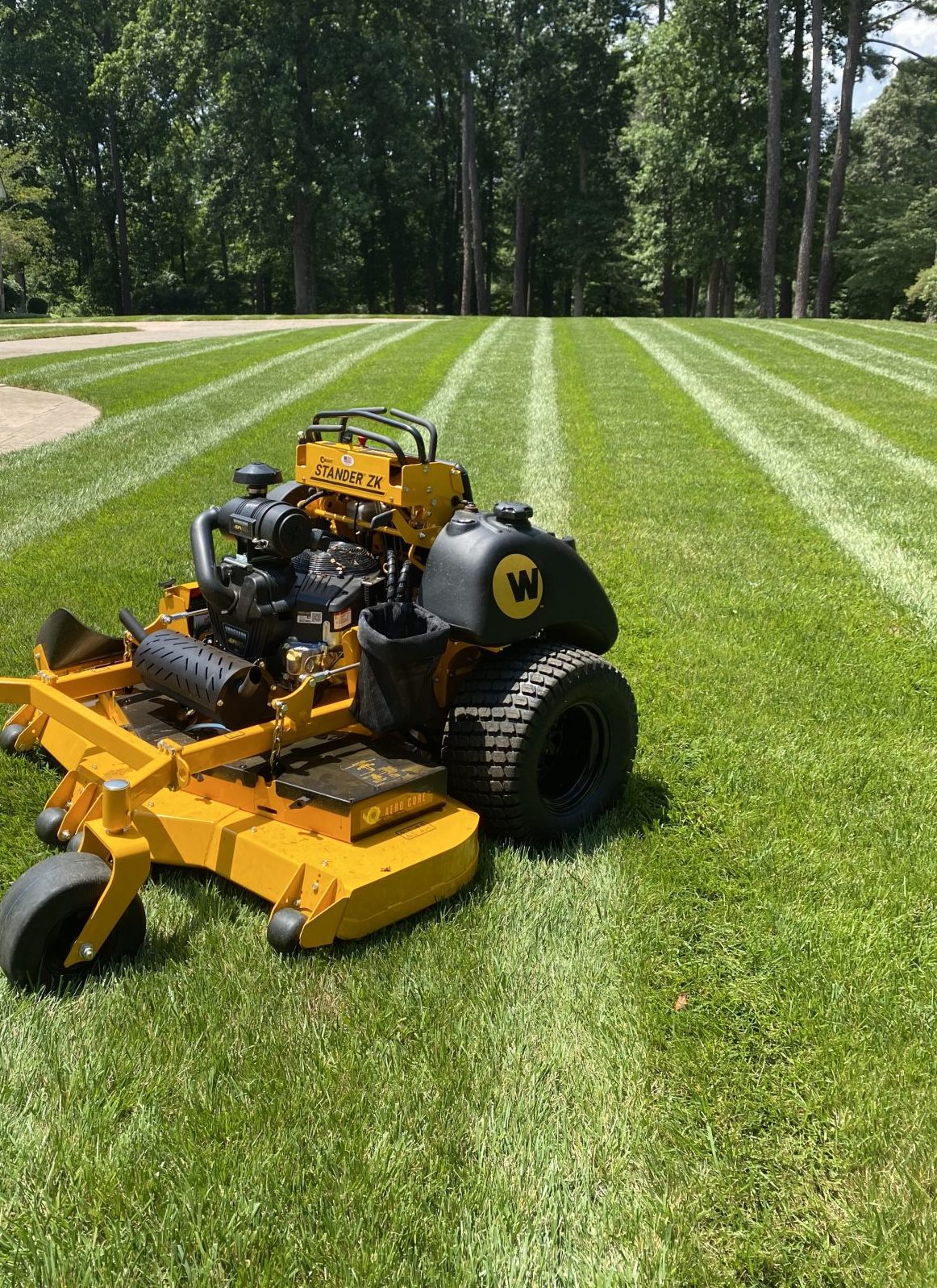Yellow stand-on mower on freshly striped residential lawn