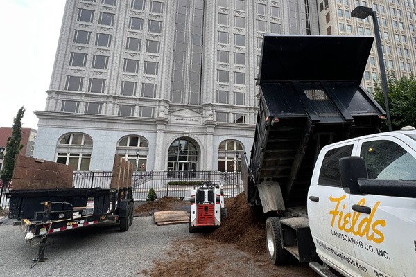 Landscaping trucks unloading mulch beside a downtown building