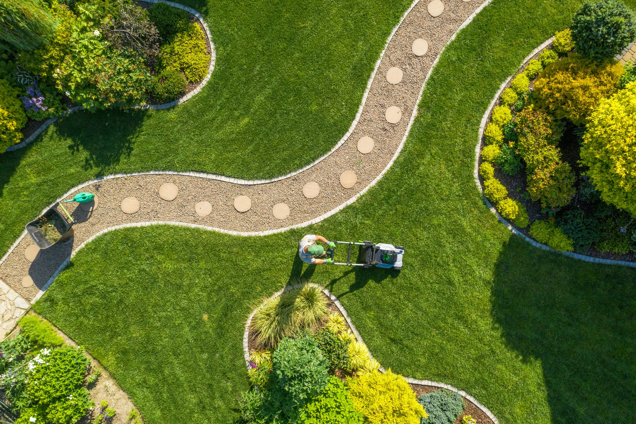 Gardener mowing lawn beside curved stepping-stone path