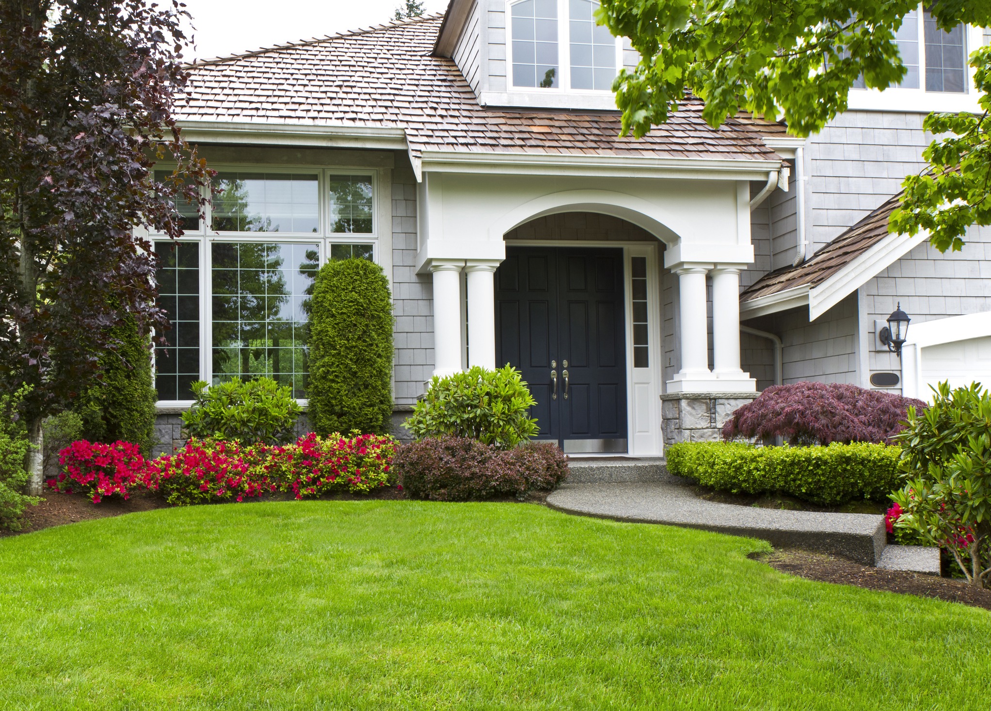 Elegant home entrance with columns, lawn, and flowering shrubs
