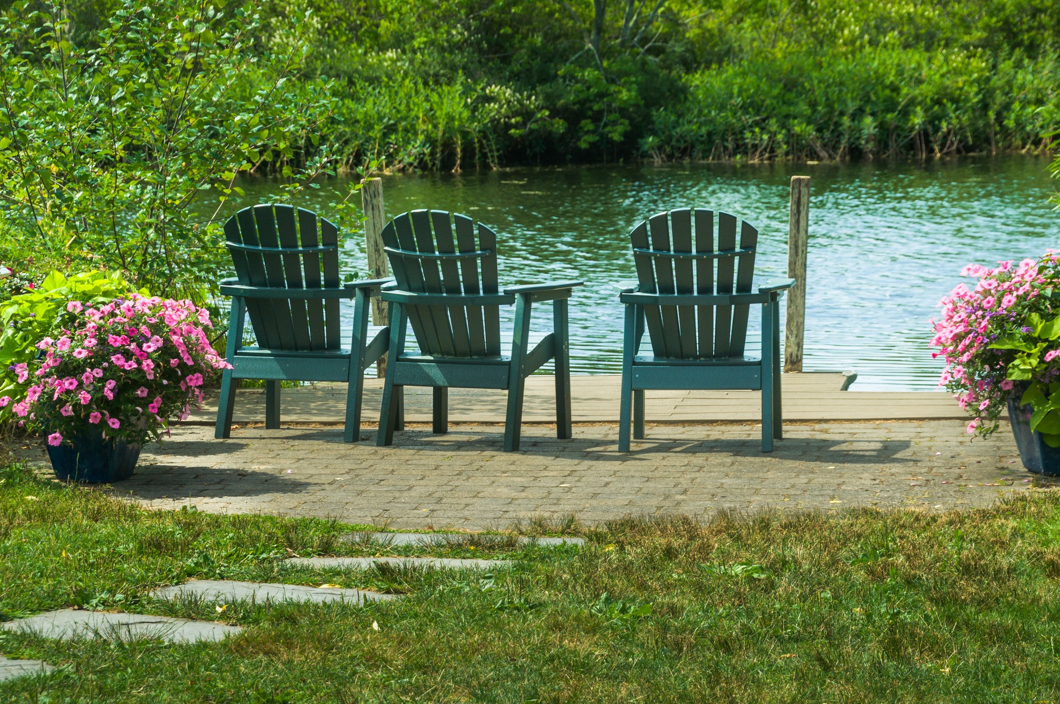 Three Adirondack chairs beside a flower-lined pond