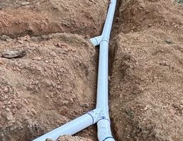 Worker installing PVC drainage pipe in backyard trench