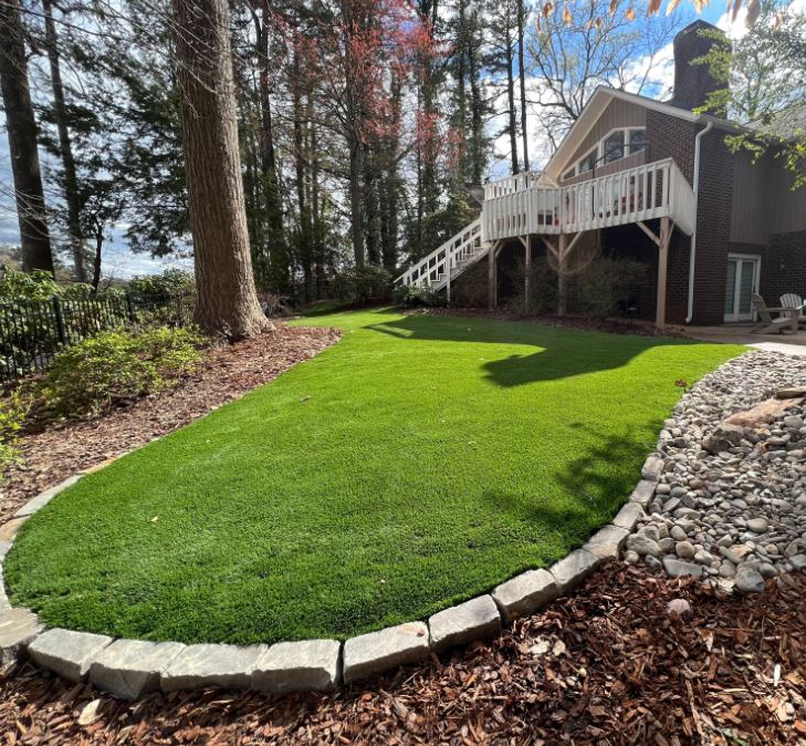 Artificial turf lawn beside wooded brick house deck