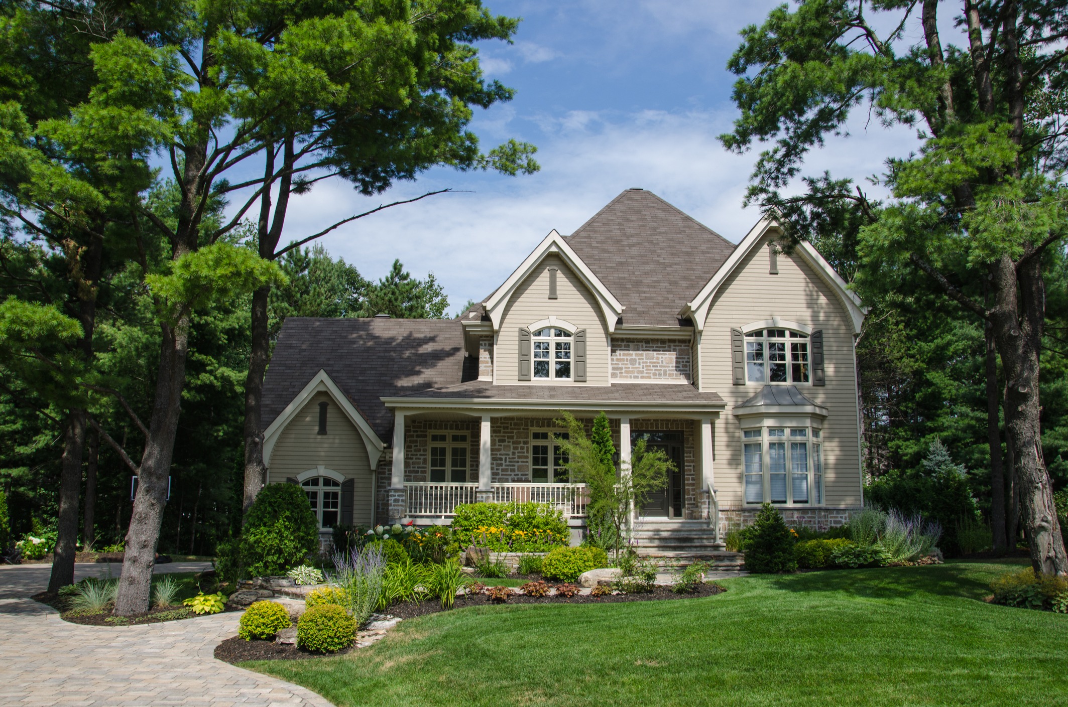 Elegant stone-front house surrounded by tall trees and gardens