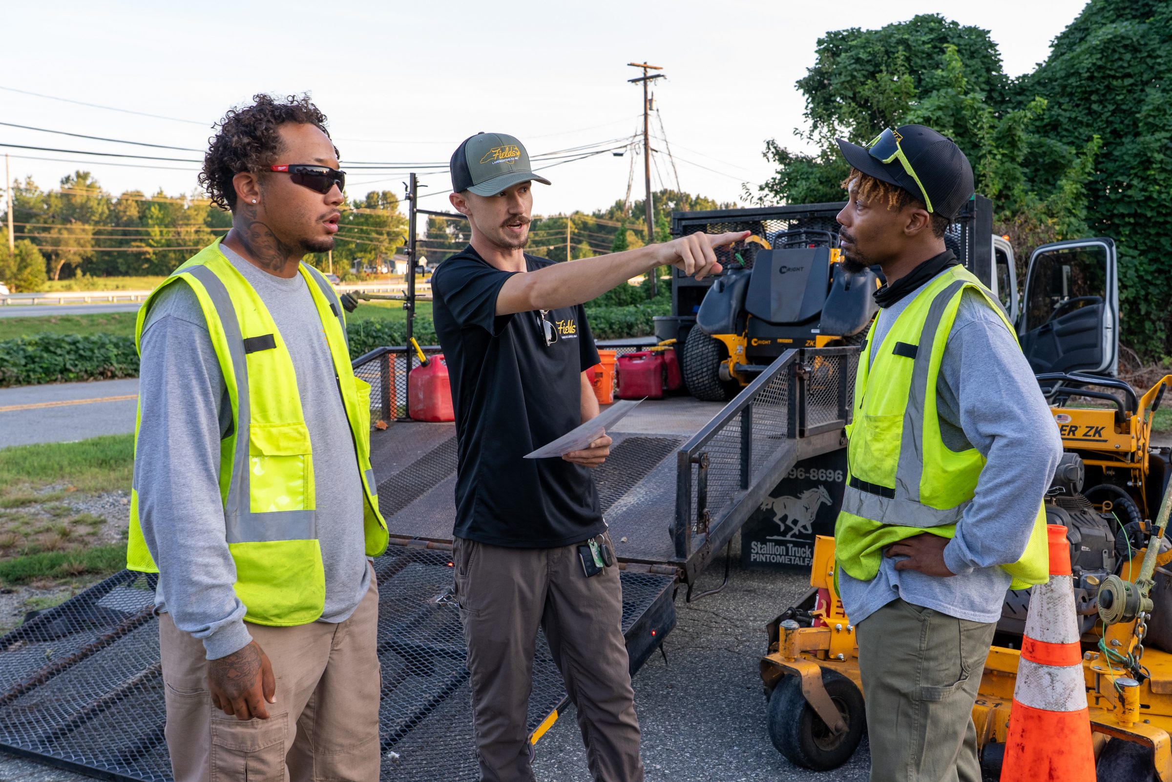 Landscaping supervisor briefs two workers beside mowing equipment