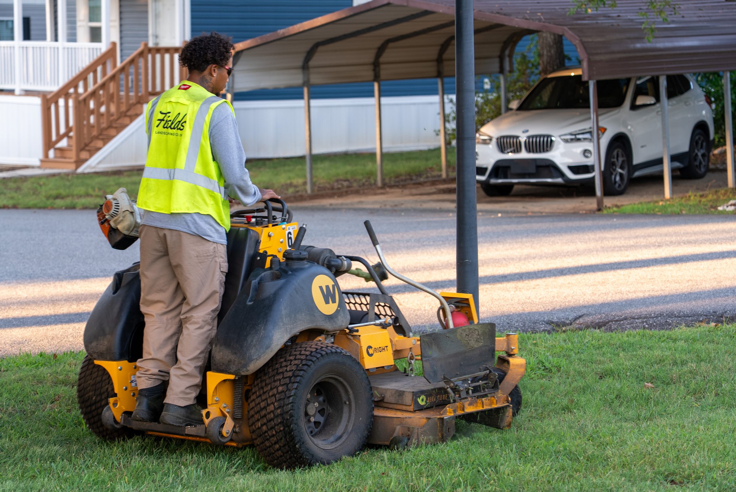 Landscaper operating a stand-on mower beside suburban homes